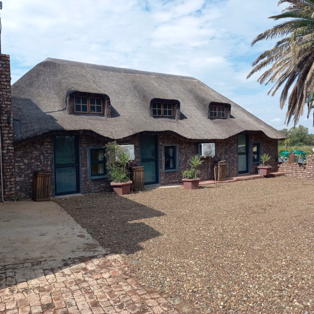 Exterior view of thatched-roof guest rooms with private entrances at Pecan Guesthouse in Christiana.