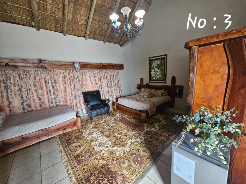 Thatched roof bedroom featuring a double bed, single daybed, and large vintage rug in Room 3.