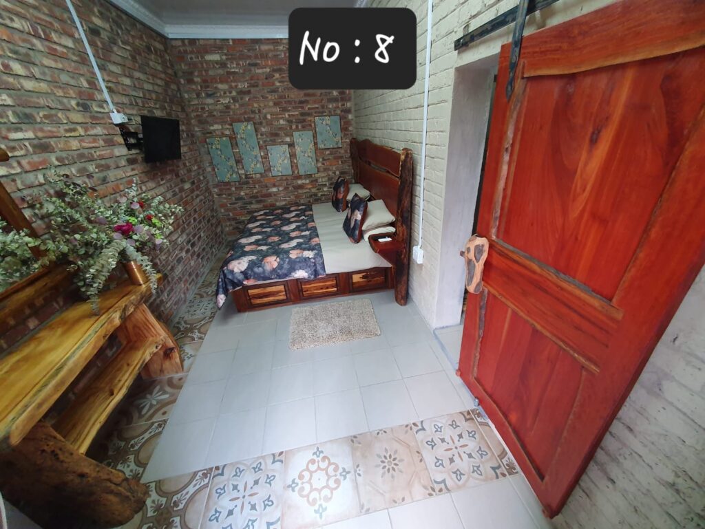 Rustic room with a live-edge wooden bed frame, patterned tiled flooring, exposed brick wall, and a heavy wooden sliding door.