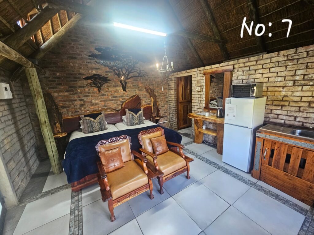 Thatched unit with tree wall art, twin beds side-by-side, leather chairs, and full kitchenette.